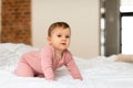 Adorable baby girl crawling on bed and looking at camera in bedroom interior, free space Royalty Free Stock Photo