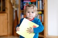 Adorable baby girl holding a book. Beautiful toddler child at home wants reading fairy tale.