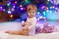 Adorable baby girl holding colorful lights garland in cute hands. Little child in festive clothes decorating Christmas Royalty Free Stock Photo