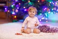 Adorable baby girl holding colorful lights garland in cute hands. Little child in festive clothes decorating Christmas Royalty Free Stock Photo