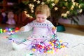 Adorable baby girl holding colorful lights garland in cute hands. Little child in festive clothes decorating Christmas