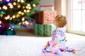 Adorable baby girl holding colorful lights garland in cute hands. Little child in festive clothes decorating Christmas Royalty Free Stock Photo