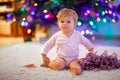 Adorable baby girl holding colorful lights garland in cute hands. Little child in festive clothes decorating Christmas