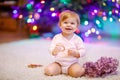 Adorable baby girl holding colorful lights garland in cute hands. Little child in festive clothes decorating Christmas Royalty Free Stock Photo