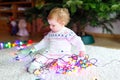 Adorable baby girl holding colorful lights garland in cute hands. Little child in festive clothes decorating Christmas