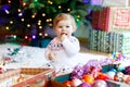 Adorable baby girl holding colorful lights garland in cute hands. Little child in festive clothes decorating Christmas