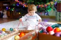 Adorable baby girl holding colorful lights garland in cute hands. Little child in festive clothes decorating Christmas