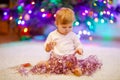 Adorable baby girl holding colorful lights garland in cute hands. Little child in festive clothes decorating Christmas