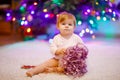 Adorable baby girl holding colorful lights garland in cute hands. Little child in festive clothes decorating Christmas