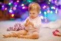 Adorable baby girl holding colorful lights garland in cute hands. Little child in festive clothes decorating Christmas