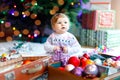 Adorable baby girl holding colorful lights garland in cute hands. Little child in festive clothes decorating Christmas Royalty Free Stock Photo
