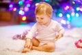 Adorable baby girl holding colorful lights garland in cute hands. Little child in festive clothes decorating Christmas