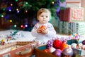 Adorable baby girl holding colorful vintage xmas toys and ball in cute hands. Little child in festive clothes decorating