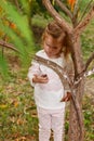 Adorable baby girl holds snail, playing in a sunny park under a tree with yellow leaves, hiding behind tree Royalty Free Stock Photo