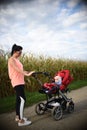 Adorable baby girl outside in red stroller in fields with mother. Infant with soother