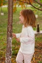Adorable baby girl playing in a sunny park under a tree with yellow leaves, hiding behind tree Royalty Free Stock Photo