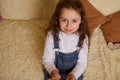 Adorable baby girl, sweetly smiling a beautiful toothy smile looking at camera, sitting on a comfy sofa at home interior