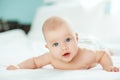 Adorable baby girl in white sunny bedroom. Newborn child relaxing and laying on belly on bed. Nursery for young children. Textile Royalty Free Stock Photo