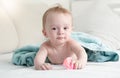 Adorable baby lying under blue towel on bed and holding plastic Royalty Free Stock Photo