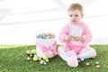 Baby in pink fluffy costume sitting on green grass near box with colorful Easter eggs isolated on white Royalty Free Stock Photo