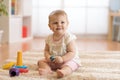 Adorable baby playing with colorful rainbow toy pyramid sitting on rug in white sunny bedroom. Toys for little kids Royalty Free Stock Photo