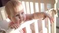 Adorable baby reach out hand in cot. Little child with interesting face Royalty Free Stock Photo