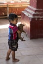 Adorable barefoot small Burmese boy seen in profile in temple holding a tiny puppy