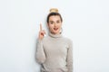 Adorable beautiful young woman with hair bun in sweater gets good idea in mind raised forefinger on isolated white background.