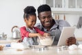 Adorable black father and daughter baking together, using digital tablet Royalty Free Stock Photo