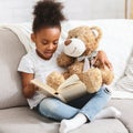 Adorable black kid with teddy bear reading book Royalty Free Stock Photo