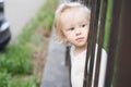 Adorable blomde baby girl is walking outdoors near the fence