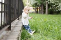 Adorable blomde baby girl is walking outdoors near the fence