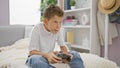 Adorable blond boy comfortably sitting on sofa at home, intensely playing a video game, fully immersed in his relaxed lifestyle Royalty Free Stock Photo