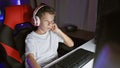 Adorable blond boy streamer, engrossed playing a futuristic video game, streaming live from his digital gaming room at night using Royalty Free Stock Photo