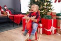 Adorable blond toddler playing with reindeer rocking by christmas tree at home