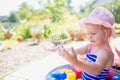 Adorable blonde baby girl 3 year old in a pink hat and blue stripped swimsuit having bath at backyard and playing with bubbles