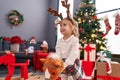 Adorable blonde girl playing with horse toy standing by christmas tree at home Royalty Free Stock Photo