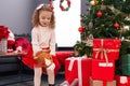 Adorable blonde girl playing with horse toy standing by christmas tree at home Royalty Free Stock Photo