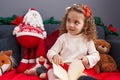 Adorable blonde girl reading book sitting on sofa by christmas decor at home Royalty Free Stock Photo
