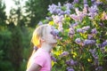 Adorable blonde girl on spring blooming bush of lillac background in a park.