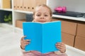 Adorable blonde girl student reading book sitting on floor at library school Royalty Free Stock Photo