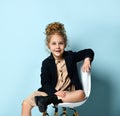 Adorable blonde girl with stylish high hairdo sitting relaxedly on an office chair showing sweet smile. Royalty Free Stock Photo