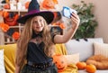 Adorable blonde girl wearing witch costume make selfie by smartphone at home