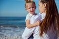 Beautiful baby girl looking at the camera, sitting on the arms of her mother carrying her while walking along the beach Royalty Free Stock Photo