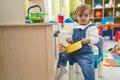 Adorable blonde toddler playing with play kitchen sitting on chair at kindergarten Royalty Free Stock Photo