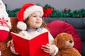 Adorable blonde toddler reading book sitting on sofa by christmas decoration at home Royalty Free Stock Photo