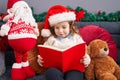 Adorable blonde toddler reading book sitting on sofa by christmas decoration at home Royalty Free Stock Photo