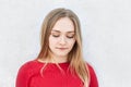 Adorable blonde woman in red dress looking thoughtfully down thinking over her relationships with boyfriend having sad expression. Royalty Free Stock Photo