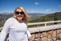 Adorable blonde woman smiles and poses for a tourist photo at the Galena Summit Overlook in the Sawtooth Mountains of Idaho