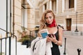 Adorable blonde woman typing message on phone standing in the middle of street. Stylish european girl in red scarf Royalty Free Stock Photo